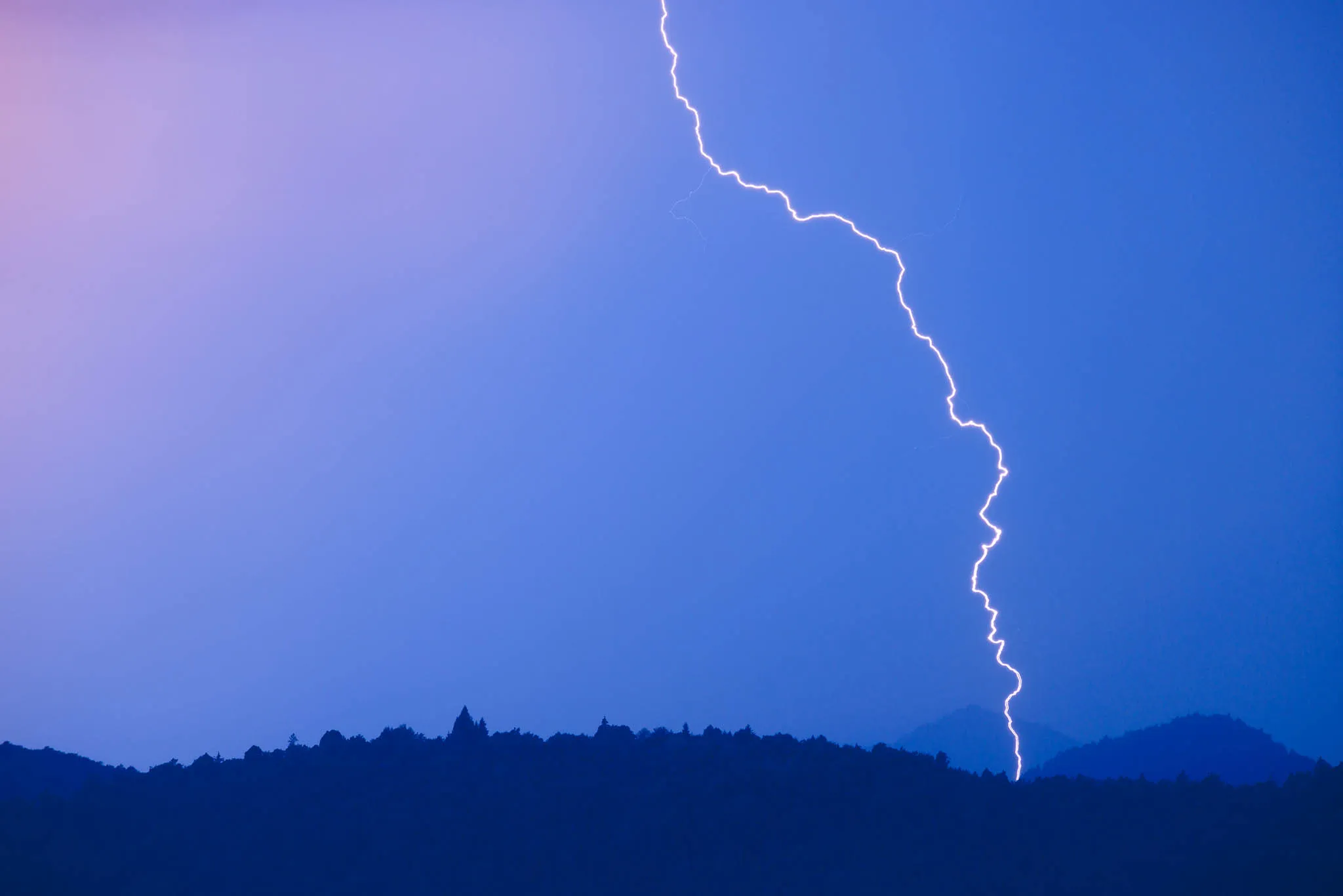 Lightining strike over hilltops at sunset
